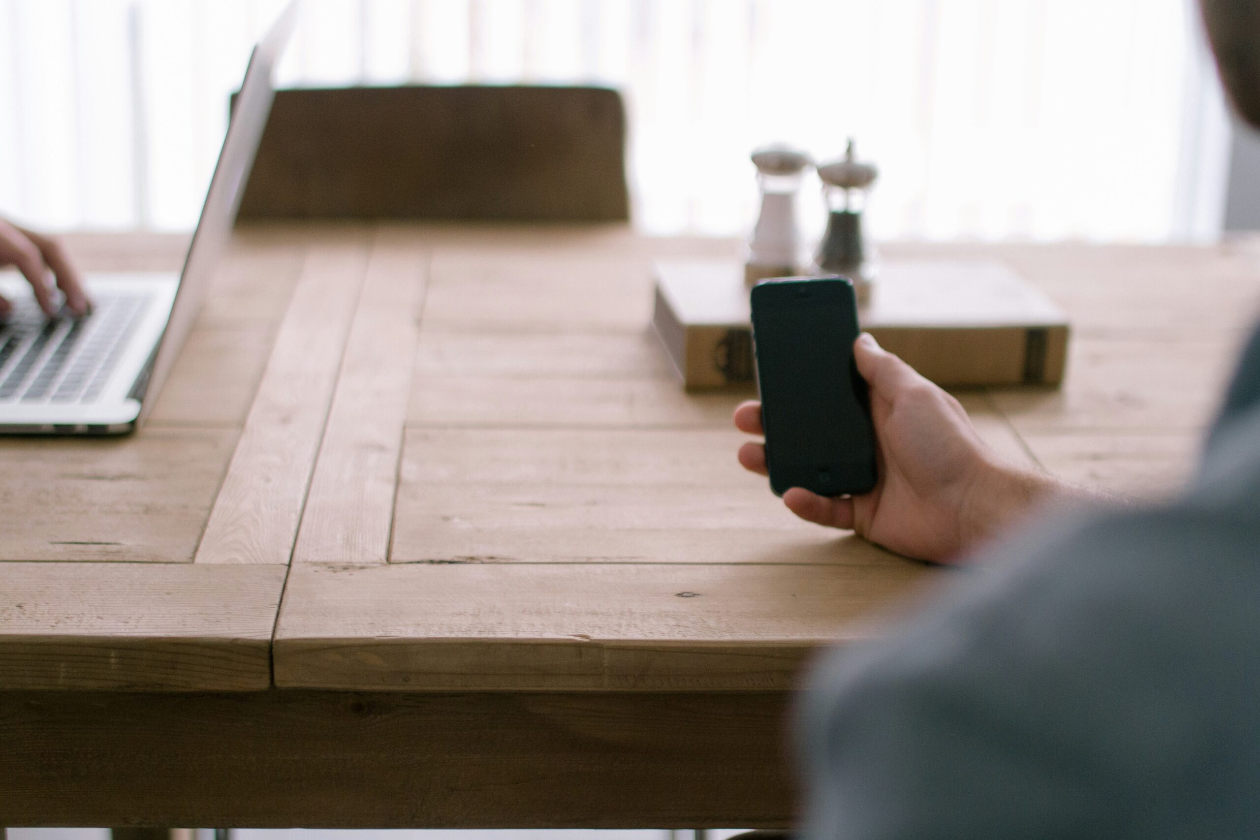 Person Holding Smartphone In Front Of Brown Table